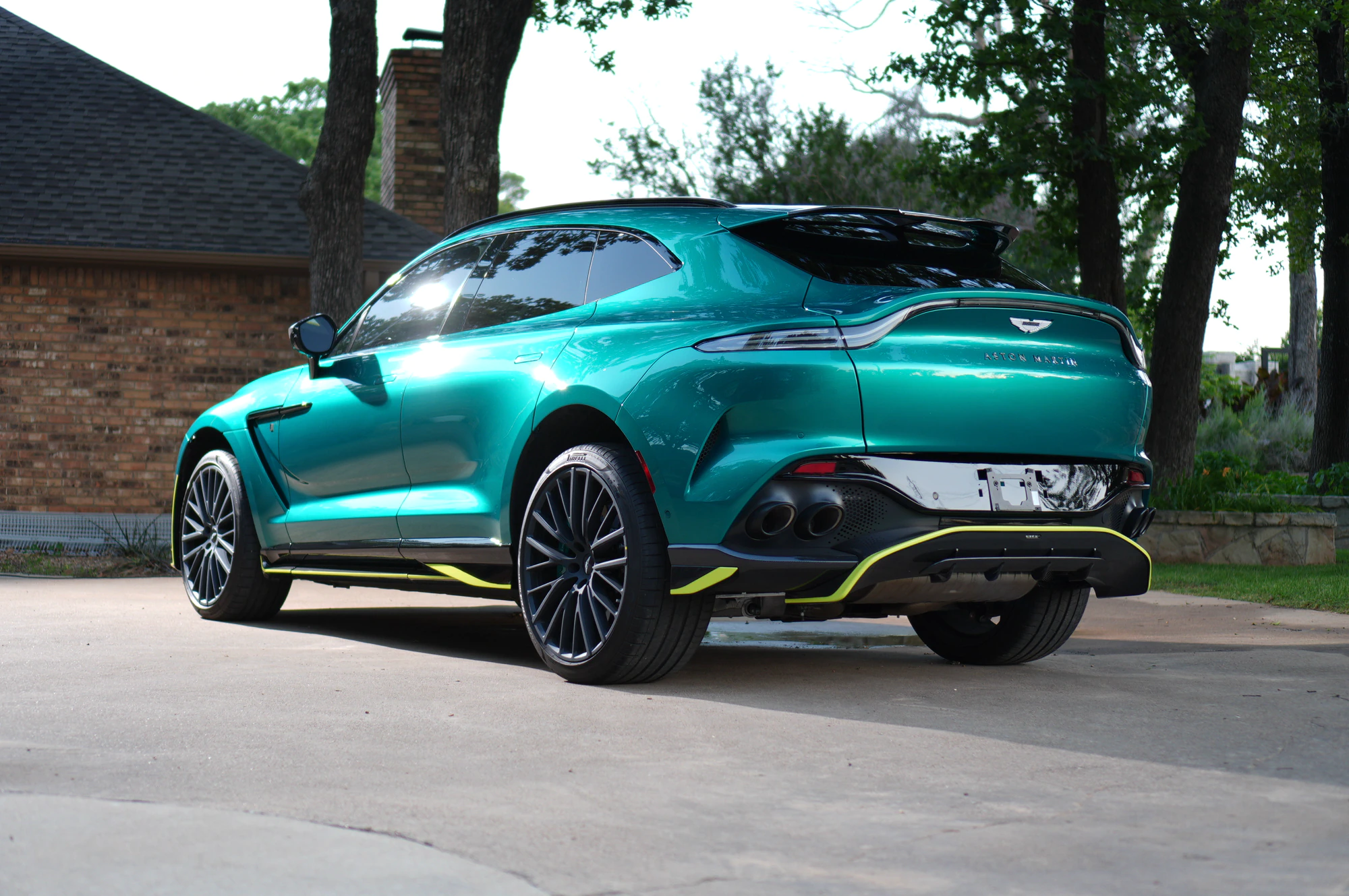 A sleek green 2024 Aston Martin DBX 707, with distinctive curves and yellow detailing, sits in the driveway. The car features large black alloy wheels and dual exhaust pipes. Expertly installed by CeramicFX, its original paint is now protected from common road hazards of North Texas by paint protection film.